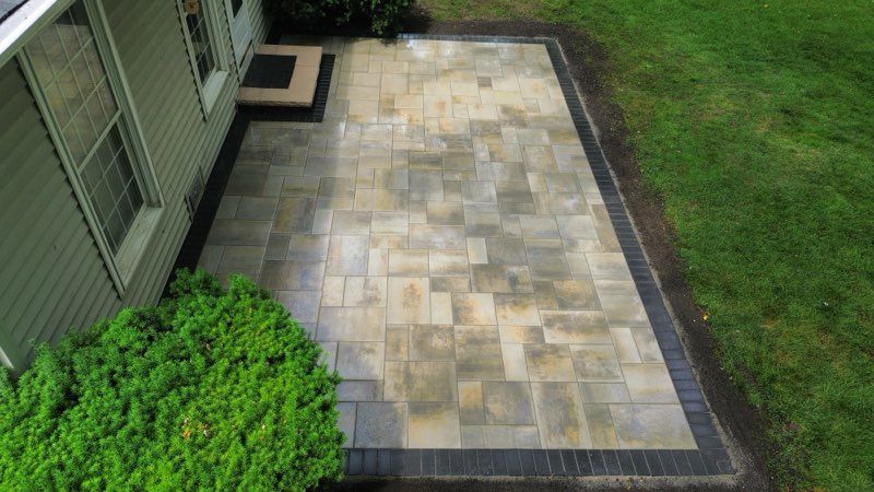 Circular brick patio with a round table and chairs, bordered by a low stone wall with flower pots and green lawn.