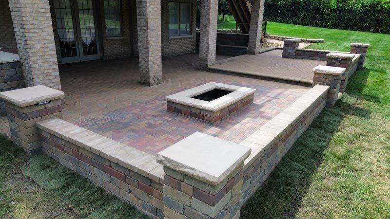 Patio with gray furniture, brick pillars, steps, and a wooden fence, on a sunny day.