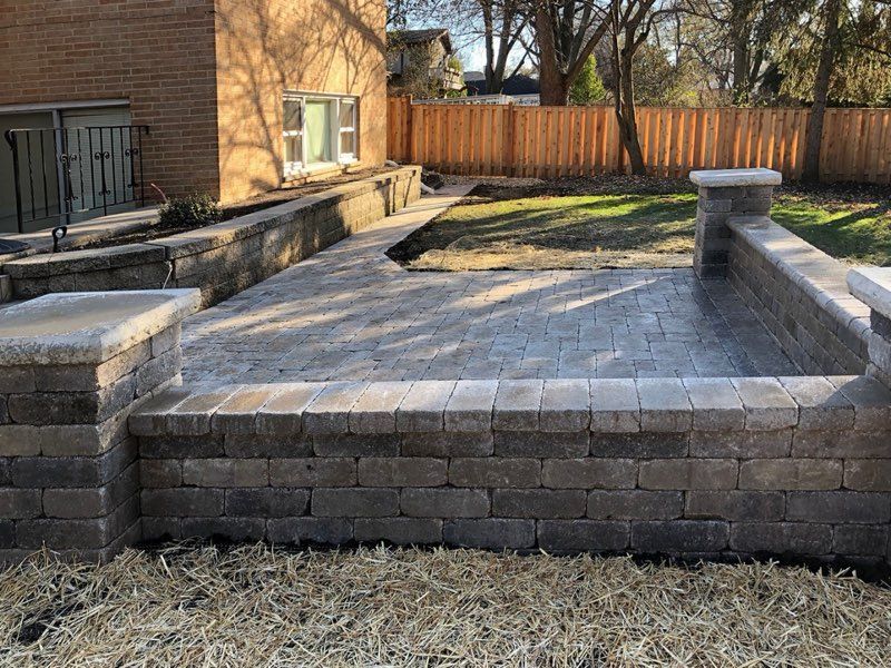 Stone brick walkway next to a landscaped garden with low stone walls and manicured green hedges.
