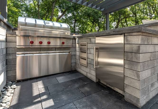 Outdoor kitchen with a grill, Big Green Egg, refrigerator, and storage on a stone patio.