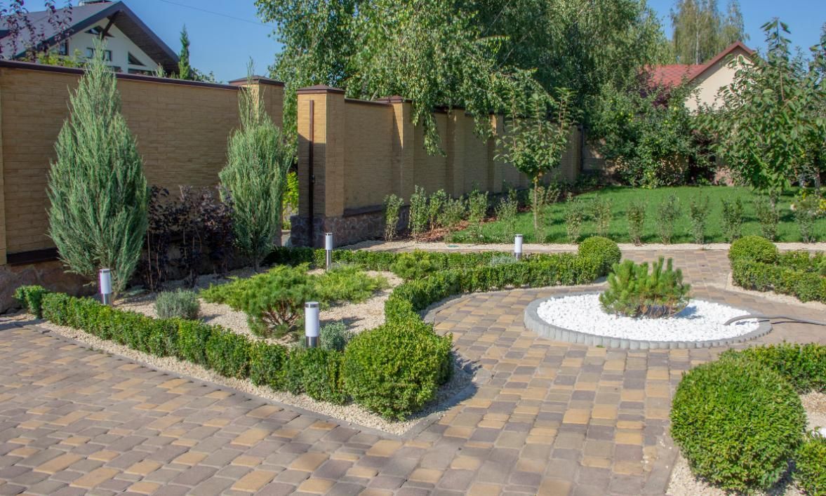 Formal garden with boxwood hedges, brick path, and small trees against a brick wall.