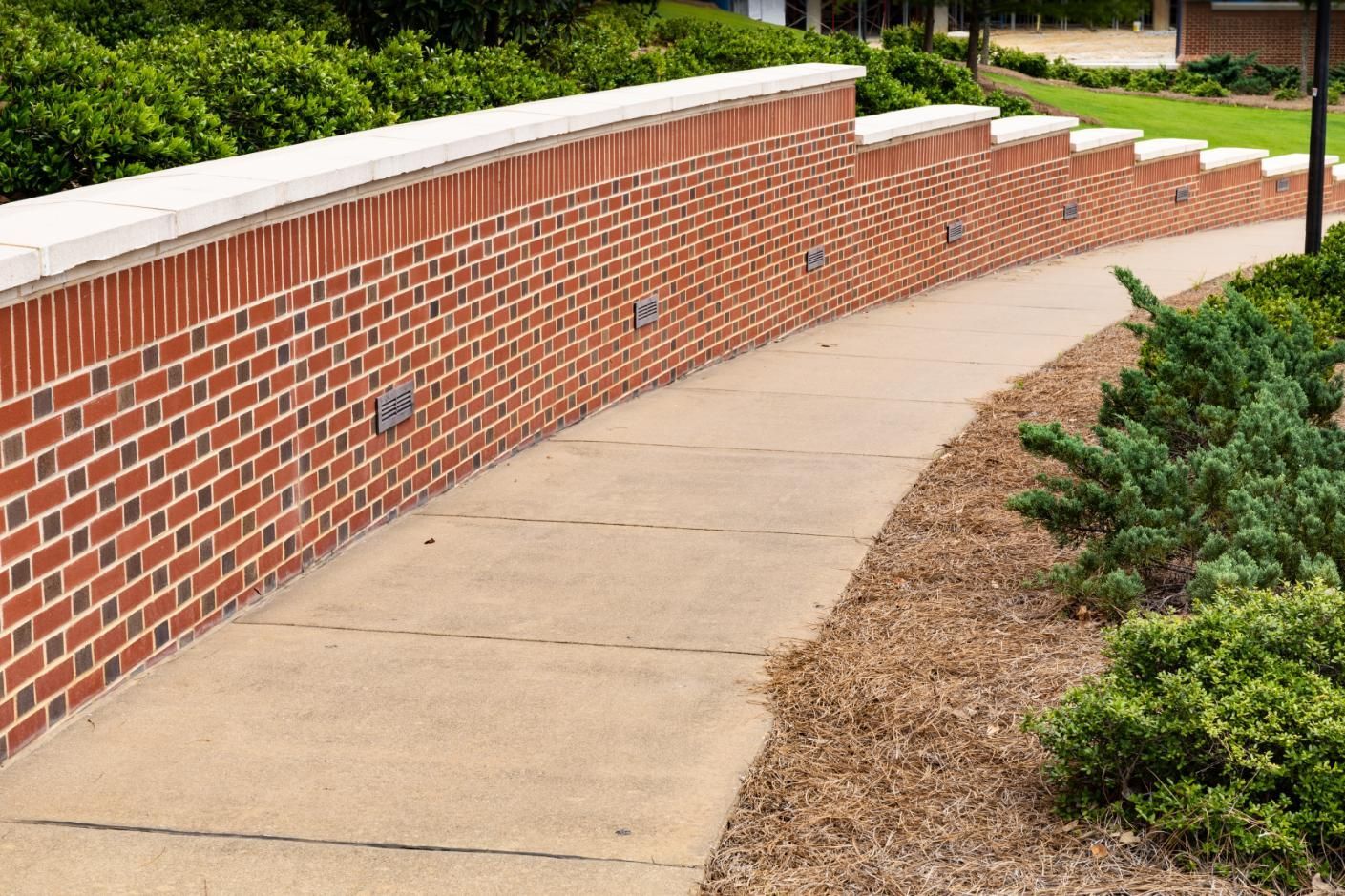 Brick wall with a concrete walkway curving through landscaping.