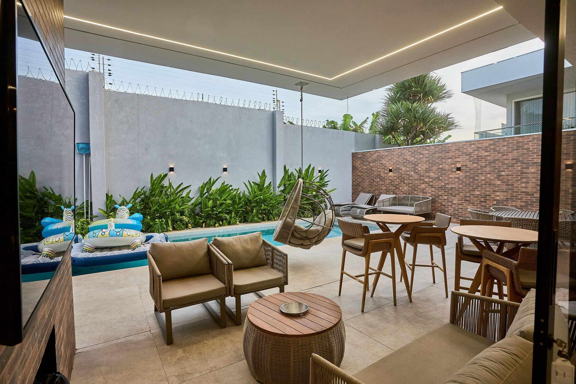 Outdoor patio with seating, small pool, and stone wall. Neutral tones, modern design, and hanging chair.