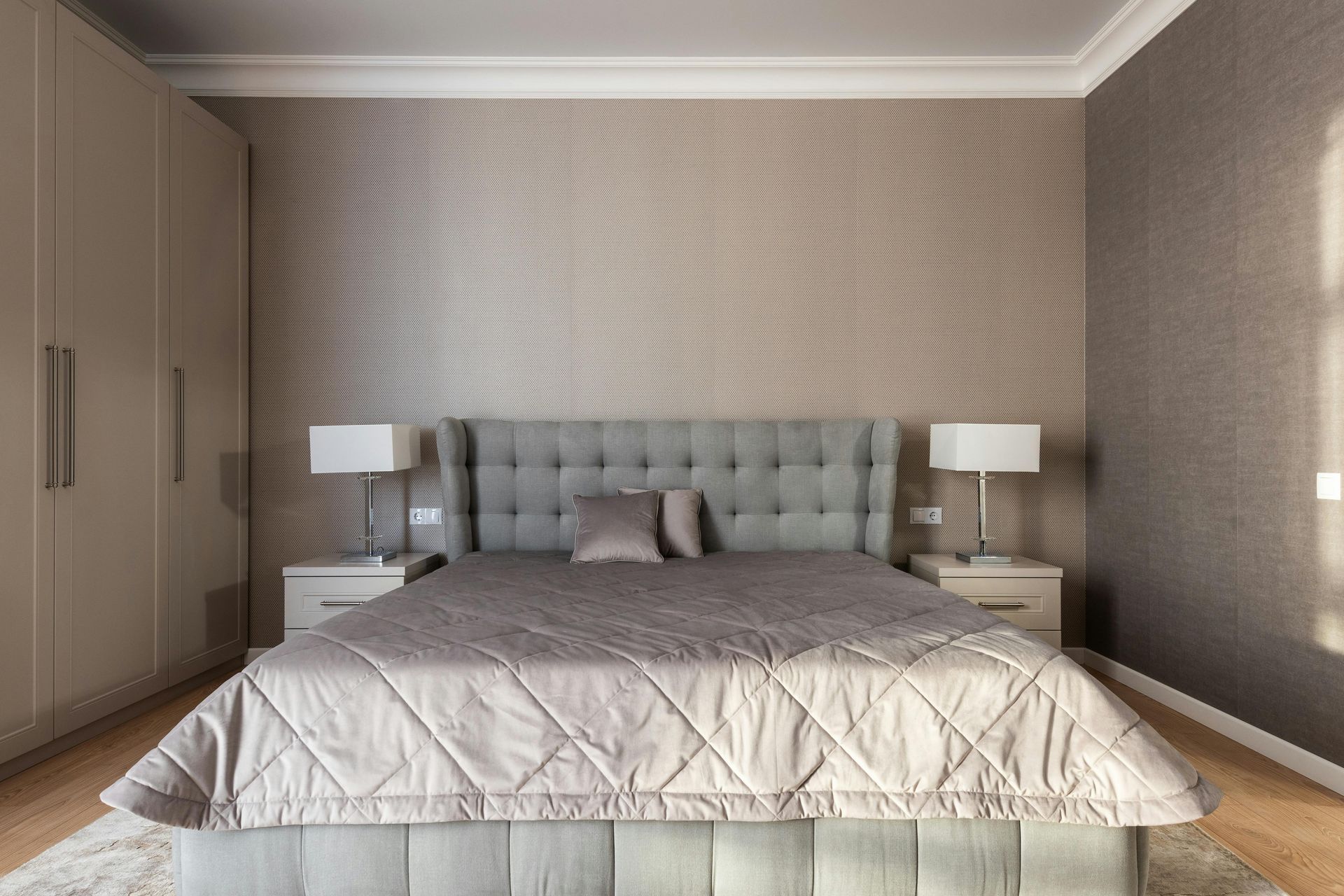 Bedroom with a gray upholstered bed, nightstands, lamps, and a large wardrobe.