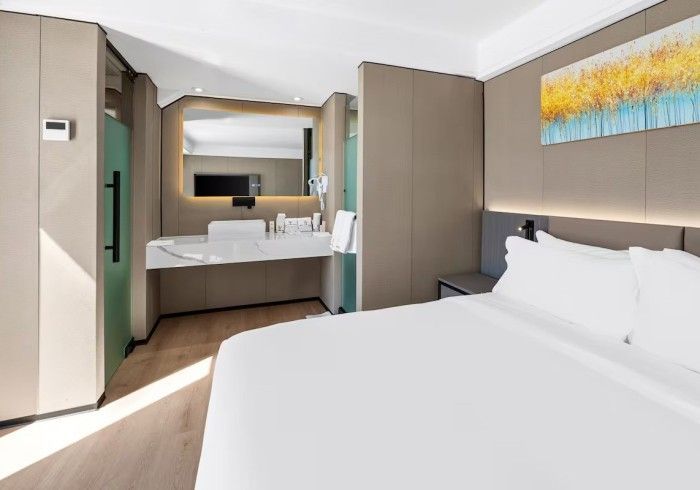 Hotel room interior with a bed, vanity, and a partially visible shower area.