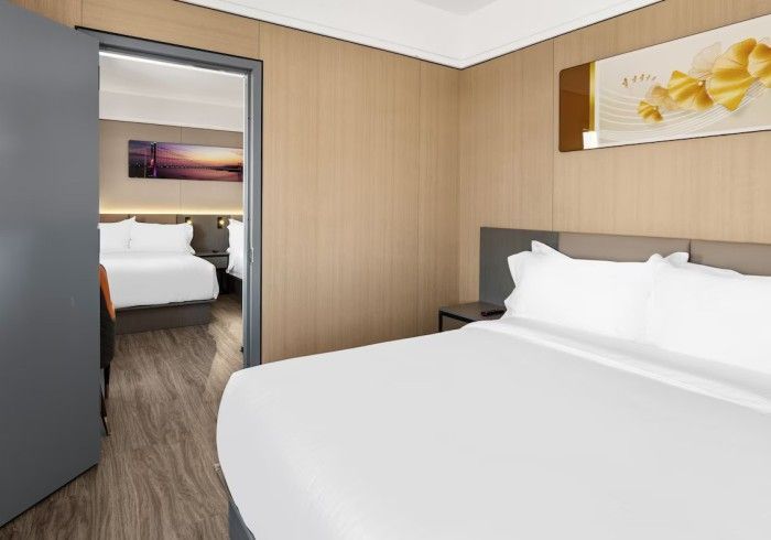 Bedroom with a bed, a door to another bedroom, light wood paneling, and a painting.