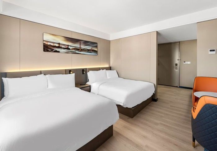 Hotel room with two beds, art, and an orange armchair.