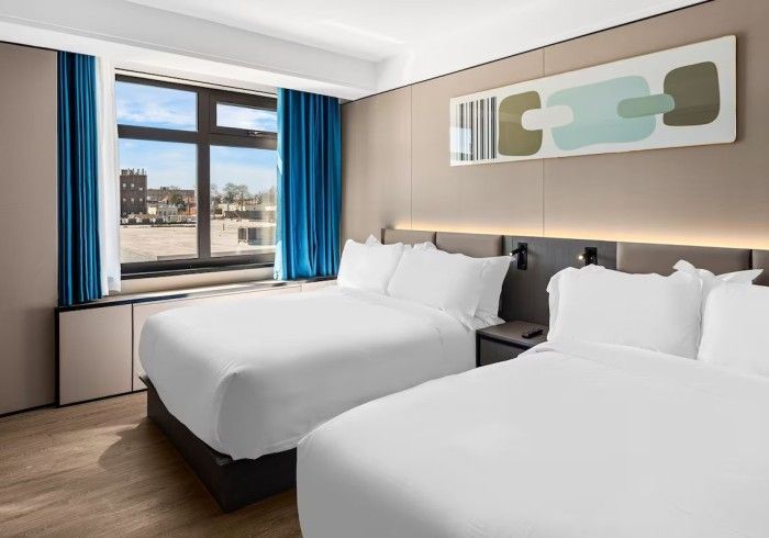 Two queen beds in a modern hotel room with a large window and blue curtains.
