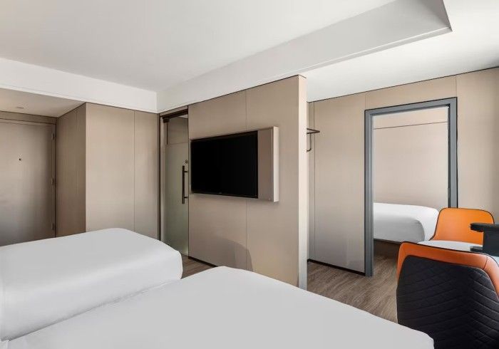 Hotel room with two beds, TV, and partial divider revealing another bed.