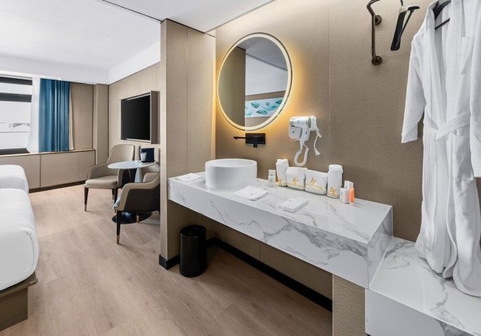 Hotel room interior: marble vanity with sink, mirror, bathrobe, TV, chair, and bed.