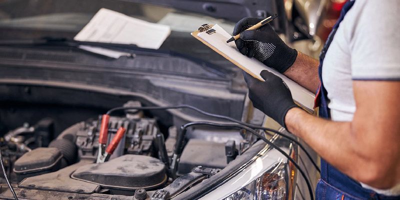 a mechanic is writing on a clipboard while working on a car .