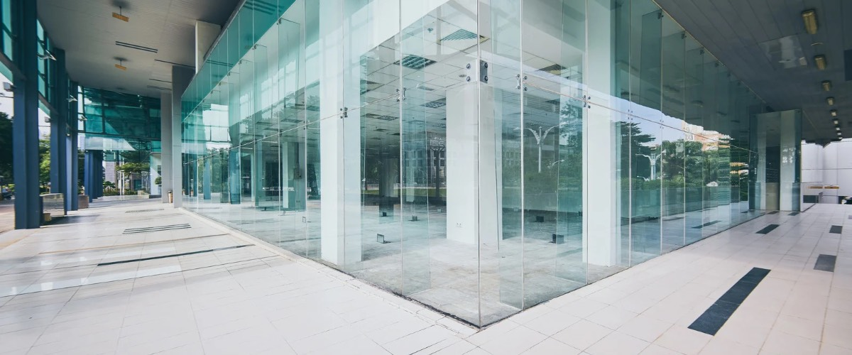 Modern glass building exterior with white pillars and a tiled walkway.