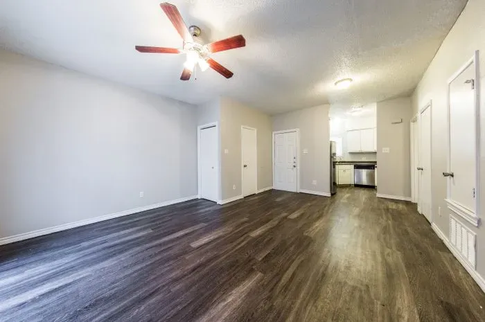 Three Villas - living room with grey laminate wood flooring and ceiling fan, looking into kitchen.
