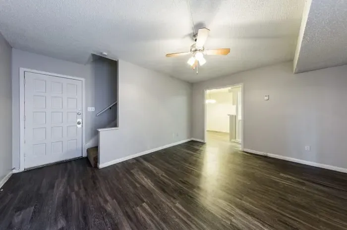 The Colony - living room with grey laminate wood flooring  with ceiling fan looking into kitchen