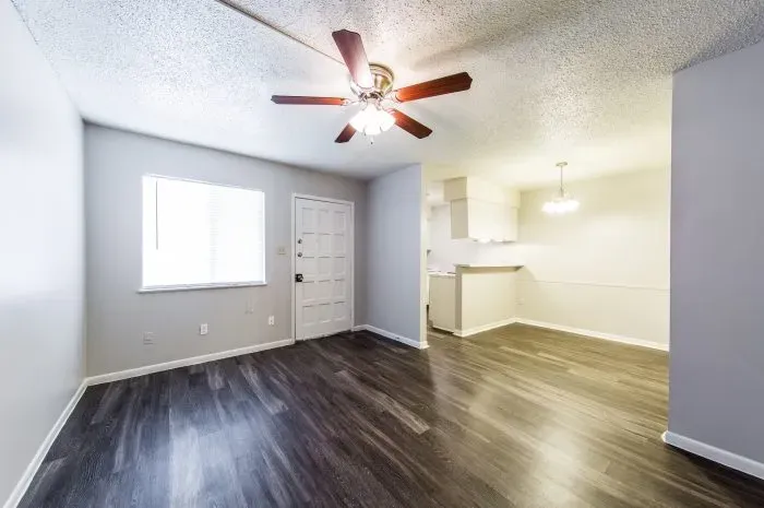 The Colony - living room with grey laminate wood flooring  with ceiling fan looking into kitchen