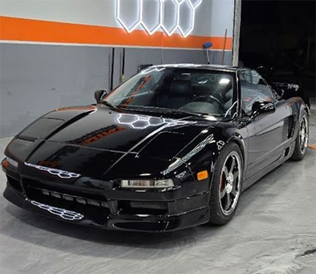 Black sports car parked indoors under bright lights, viewed from the front-left angle