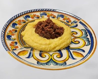 Una porzione di polenta condita con un ragù di carne scuro e denso, presentata su un piatto decorato con elaborate illustrazioni blu e oro.