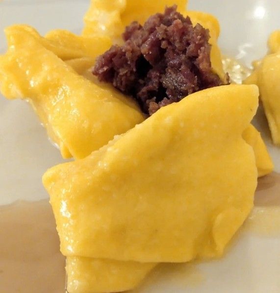 Primo piano di un impasto giallo piegato, sormontato da un cucchiaio di pasta di fagioli rosso scuro dalla consistenza particolare, su un piatto bianco.