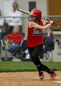 A girl in a red shirt with the letter m on it is swinging a bat