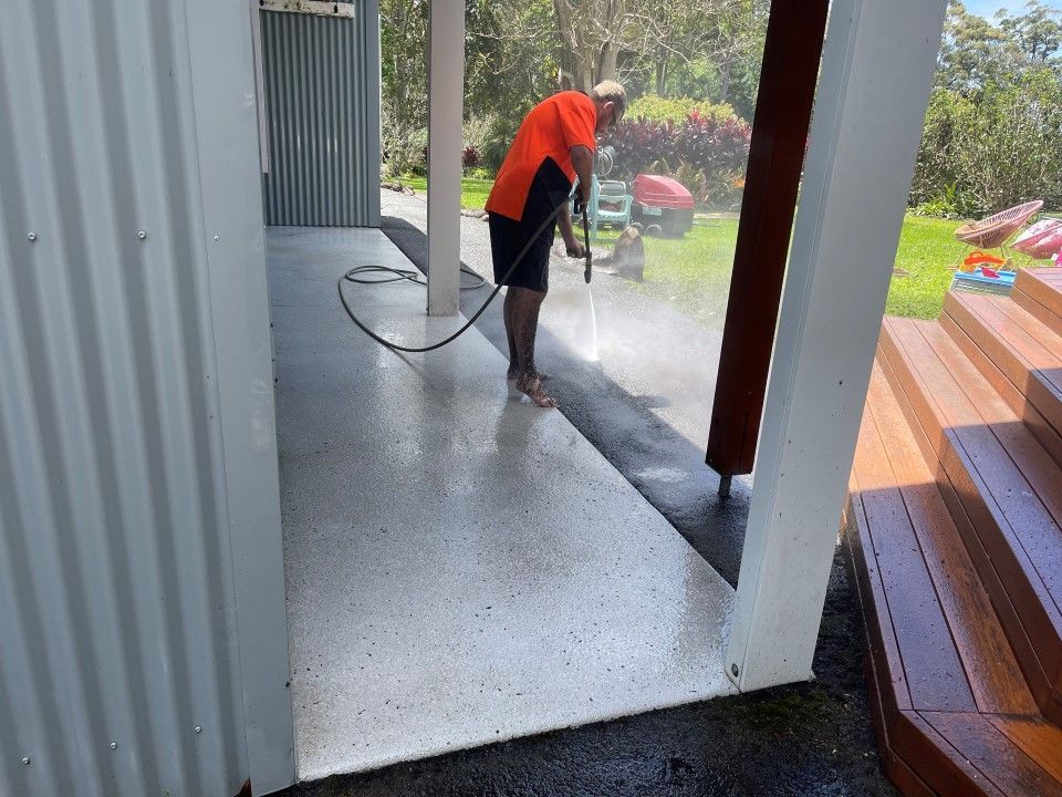 A Man is Using a High Pressure Washer to Clean a Concrete Floor — Goat Collective in Kyogle, NSW