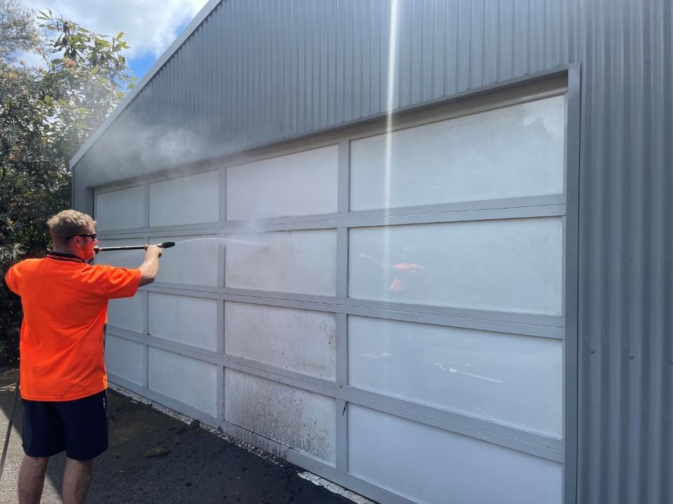 A Man is Cleaning a Garage Door With a High Pressure Washer — Goat Collective in Ballina, NSW
