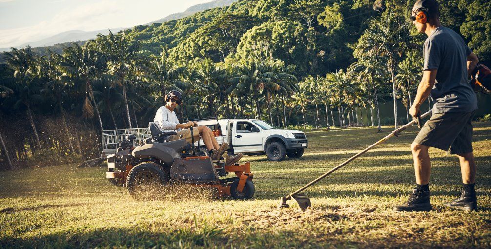 A Man is Mowing the Grass With a Lawn Mower While Another Man is Raking the Grass — Goat Collective in Tintenbar, NSW