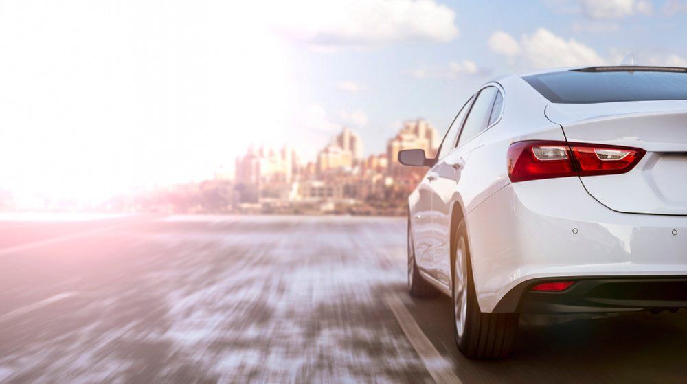 White Sedan Speeding on a Highway Towards a Blurred City Skyline — Albury Super Cheap Car Rentals in Lavington, NSW