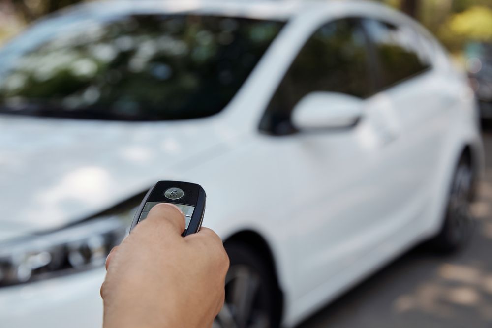 Hand Holding a Car Key Remote, Pressing a Button Towards a White Car — Albury Super Cheap Car Rentals in Lavington, NSW