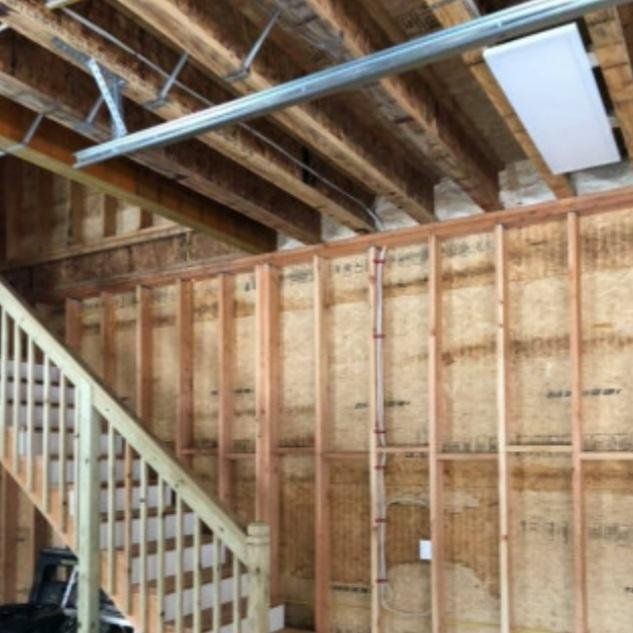 Interior view of a garage under construction, wooden beams and unfinished walls with a staircase on the left.