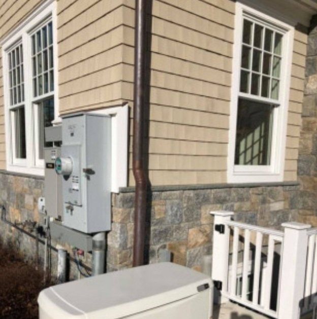 Exterior of a house with a power meter box, a generator, and windows with white frames.