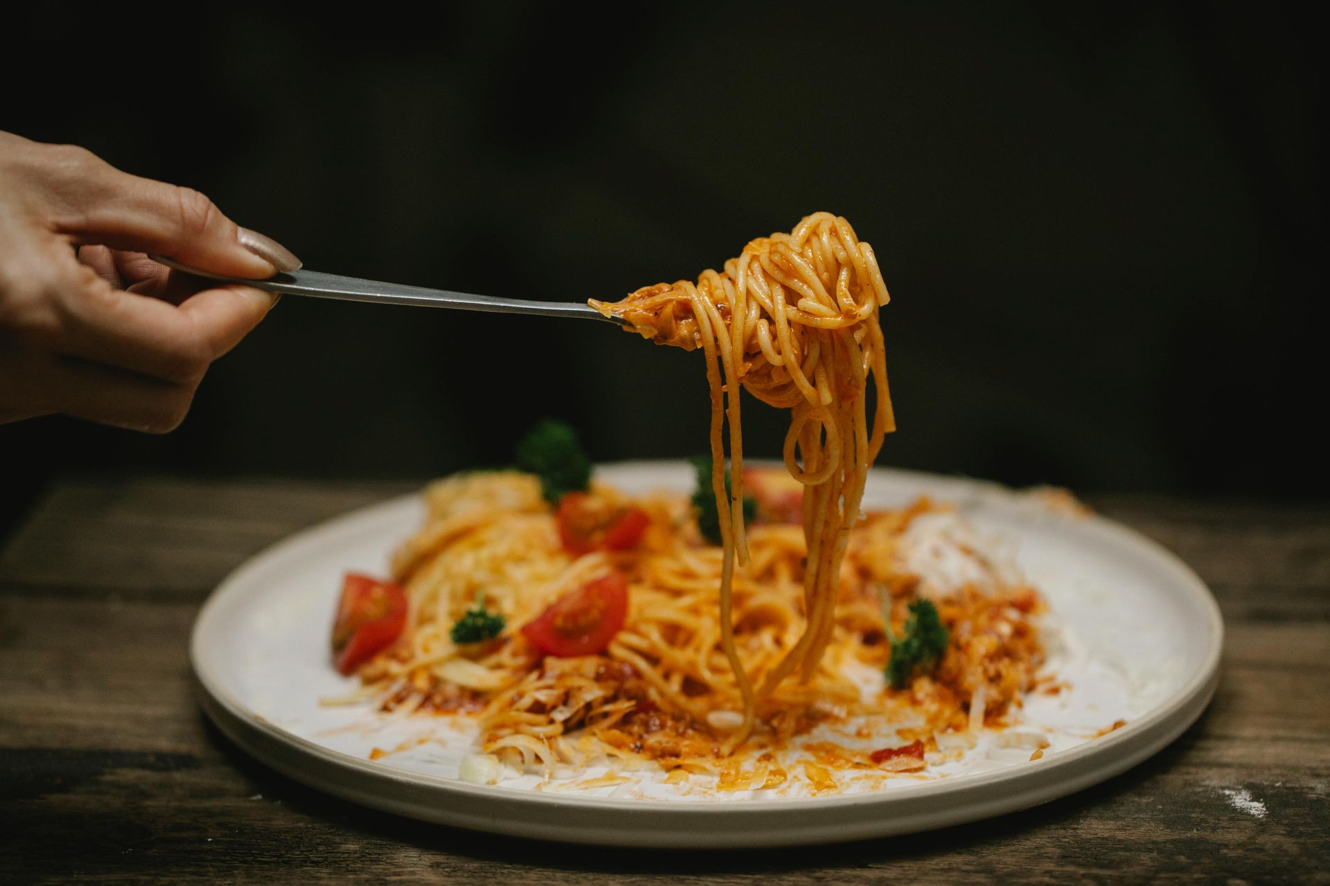 Fork holding spaghetti with red sauce, over a plate of pasta with tomatoes.