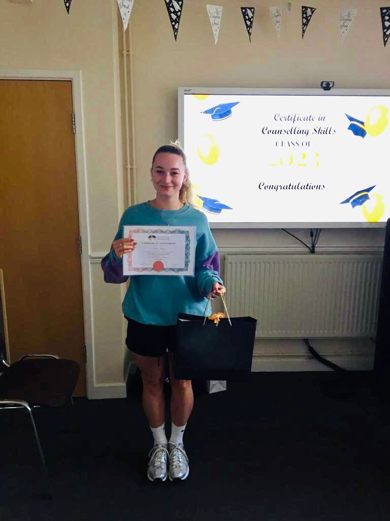 Woman holding a certificate and a bag in a room with a whiteboard and decorations.