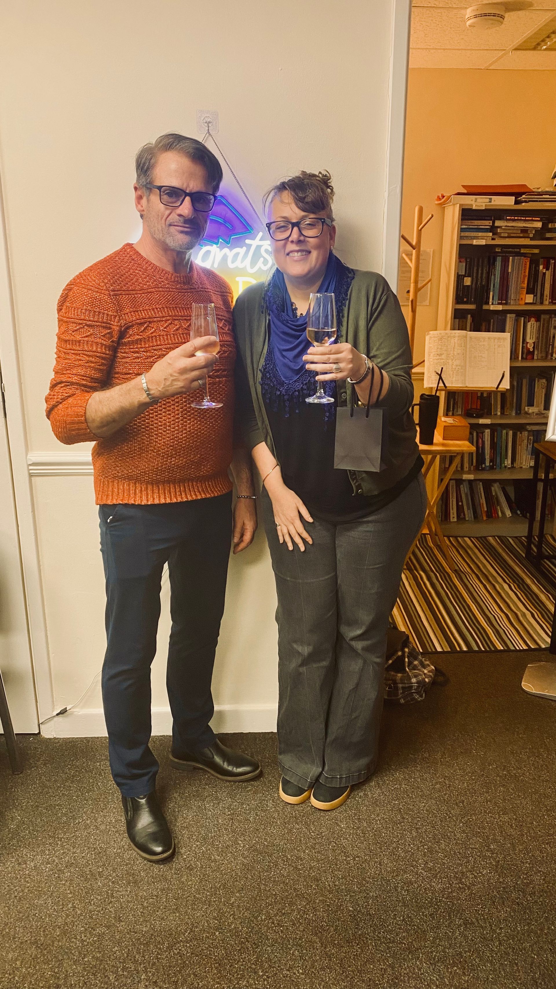 Two people clink champagne glasses in front of a 