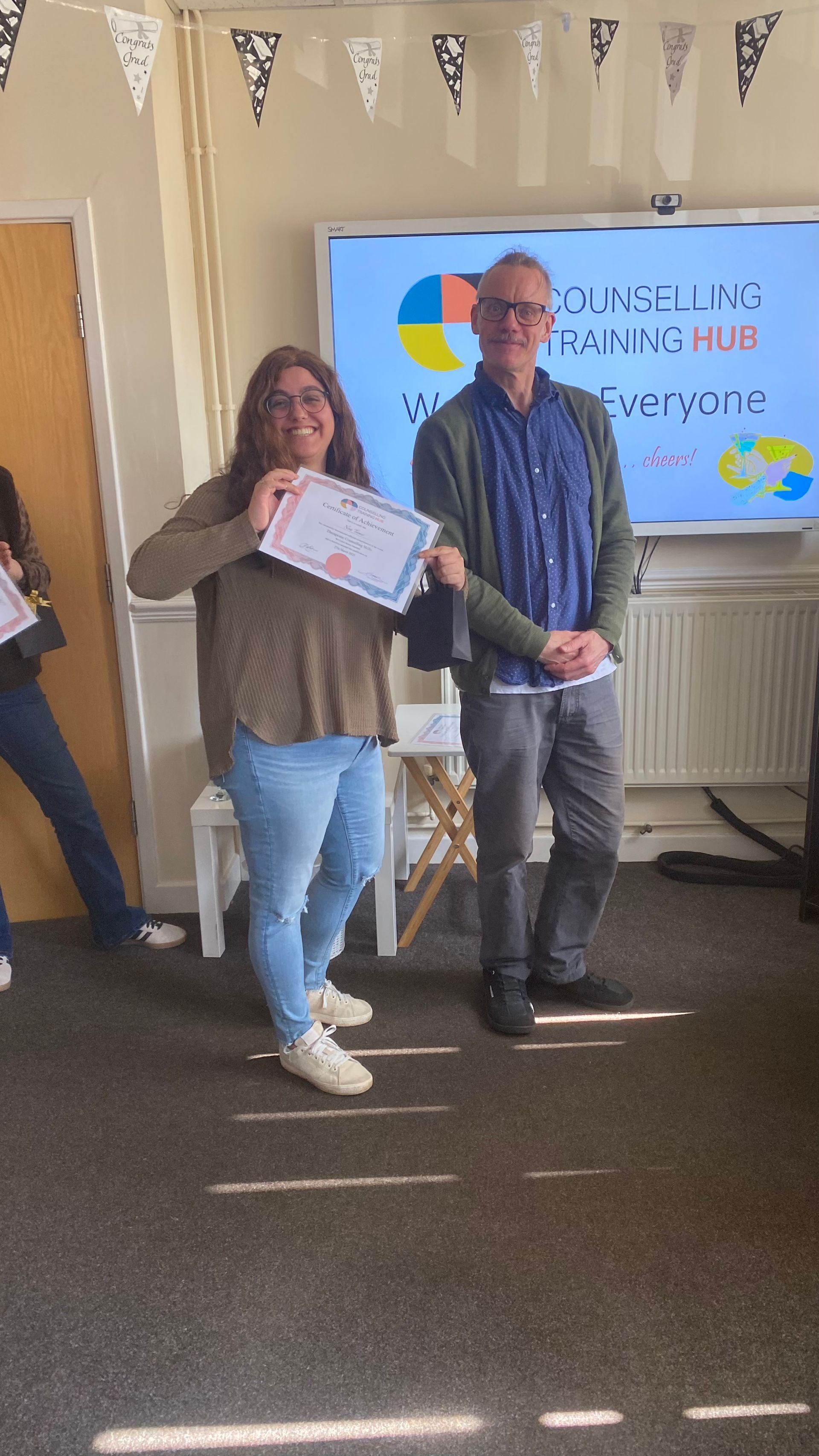 Woman receiving a certificate from a man in a training room. Whiteboard in background.