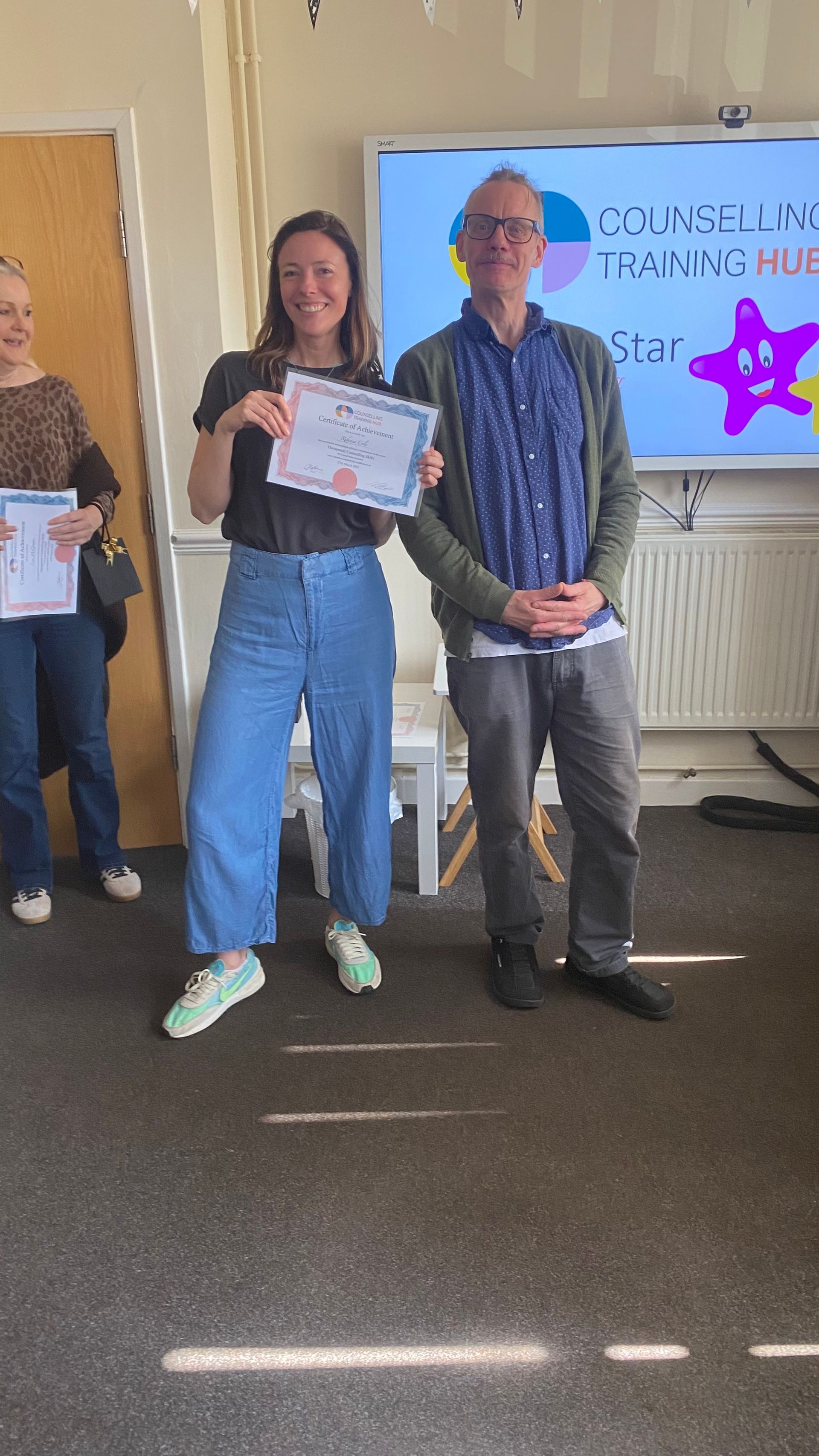 Woman holding certificate smiling, next to man with a colorful background that says 