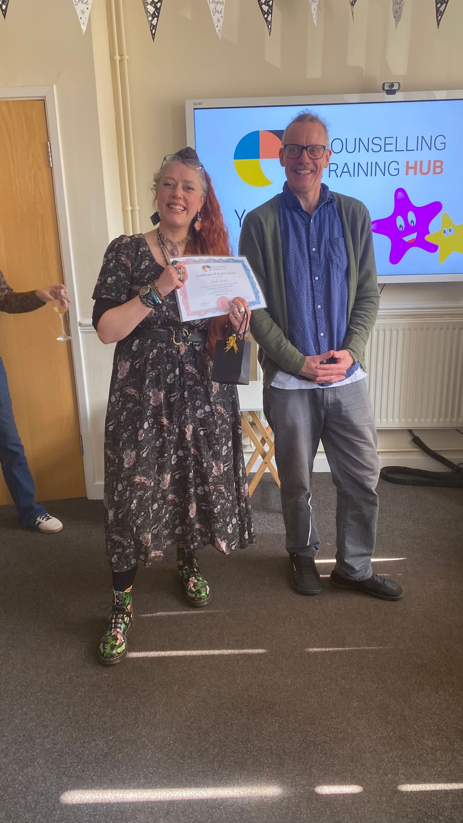 Woman in patterned dress holding a certificate smiles next to a man at a 