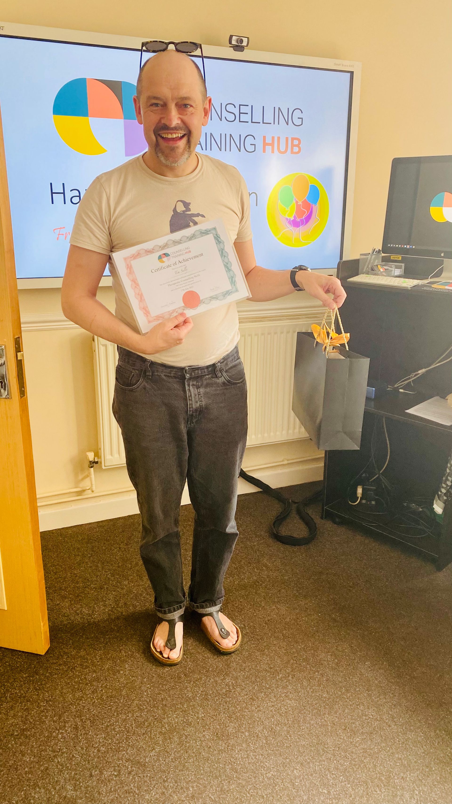 Man holding a certificate and gift bag, smiling. Standing in front of a colorful display.
