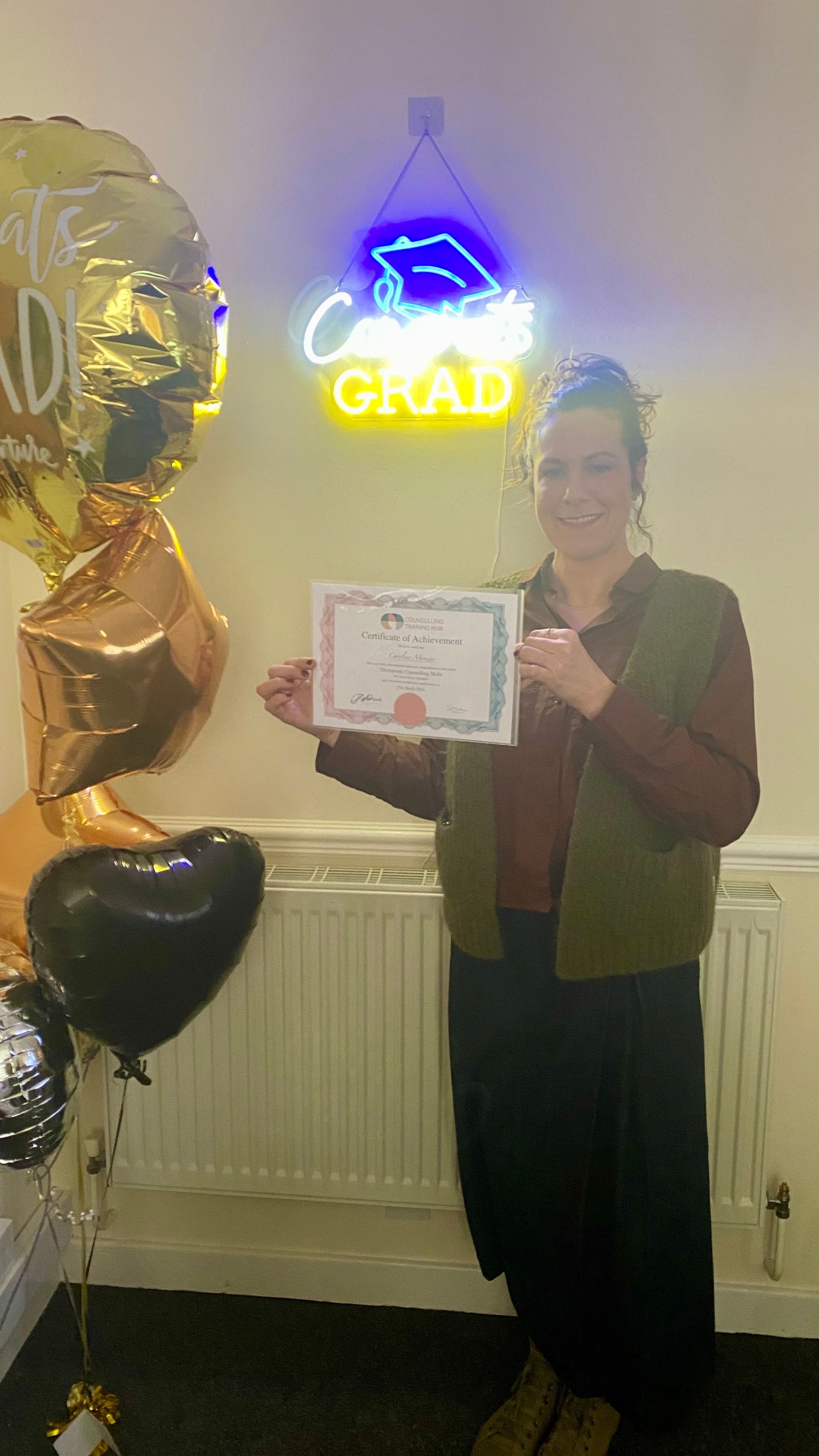 Woman holding a certificate, smiling, standing beneath a neon 