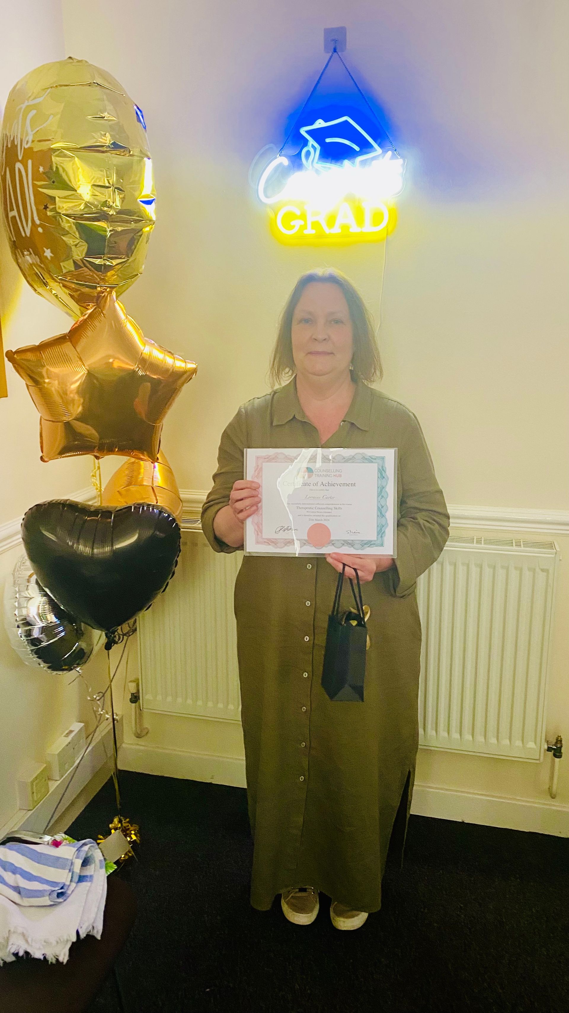 Woman in green dress holds certificate, standing by balloons and a 