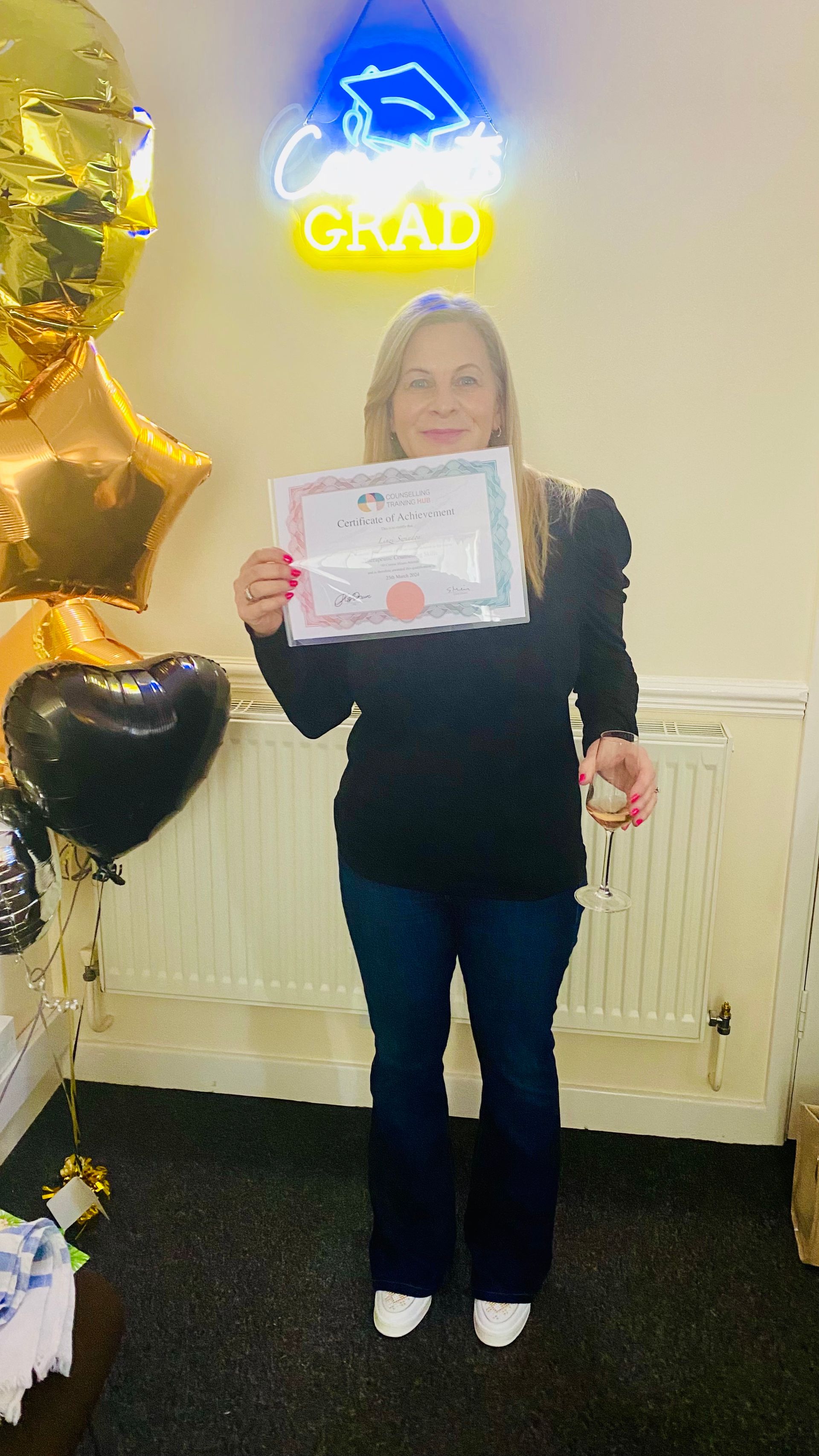 Woman holding certificate, standing in front of balloons and a neon 
