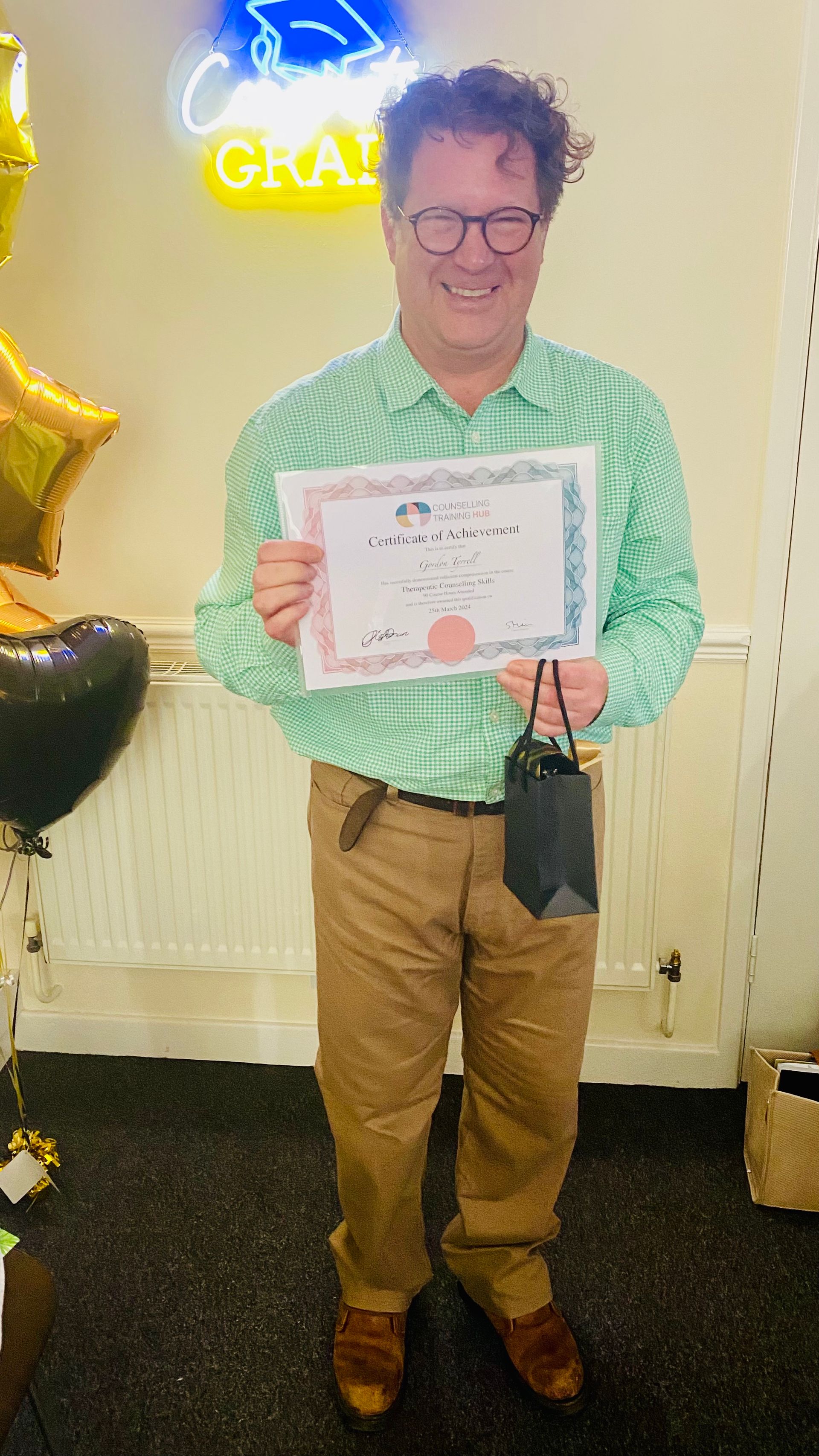 Man holding certificate and gift, smiling, in front of a neon 