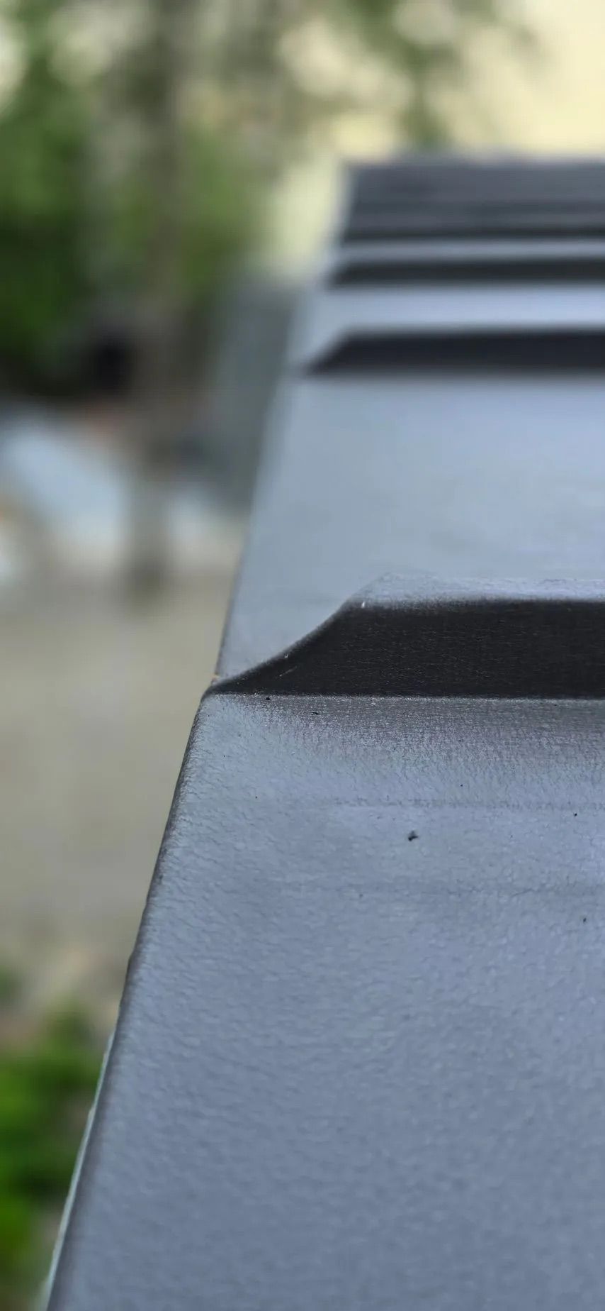 Close-up of a gray metal roof with ridges, softly blurred outdoor background