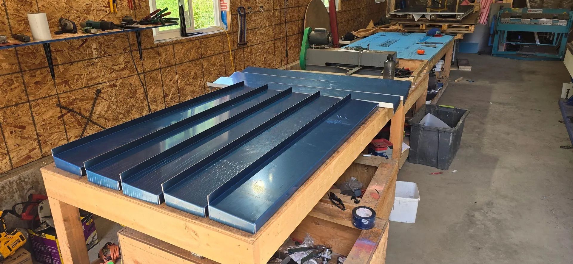 Blue metal panels on workbenches in a workshop with wood walls and tools.