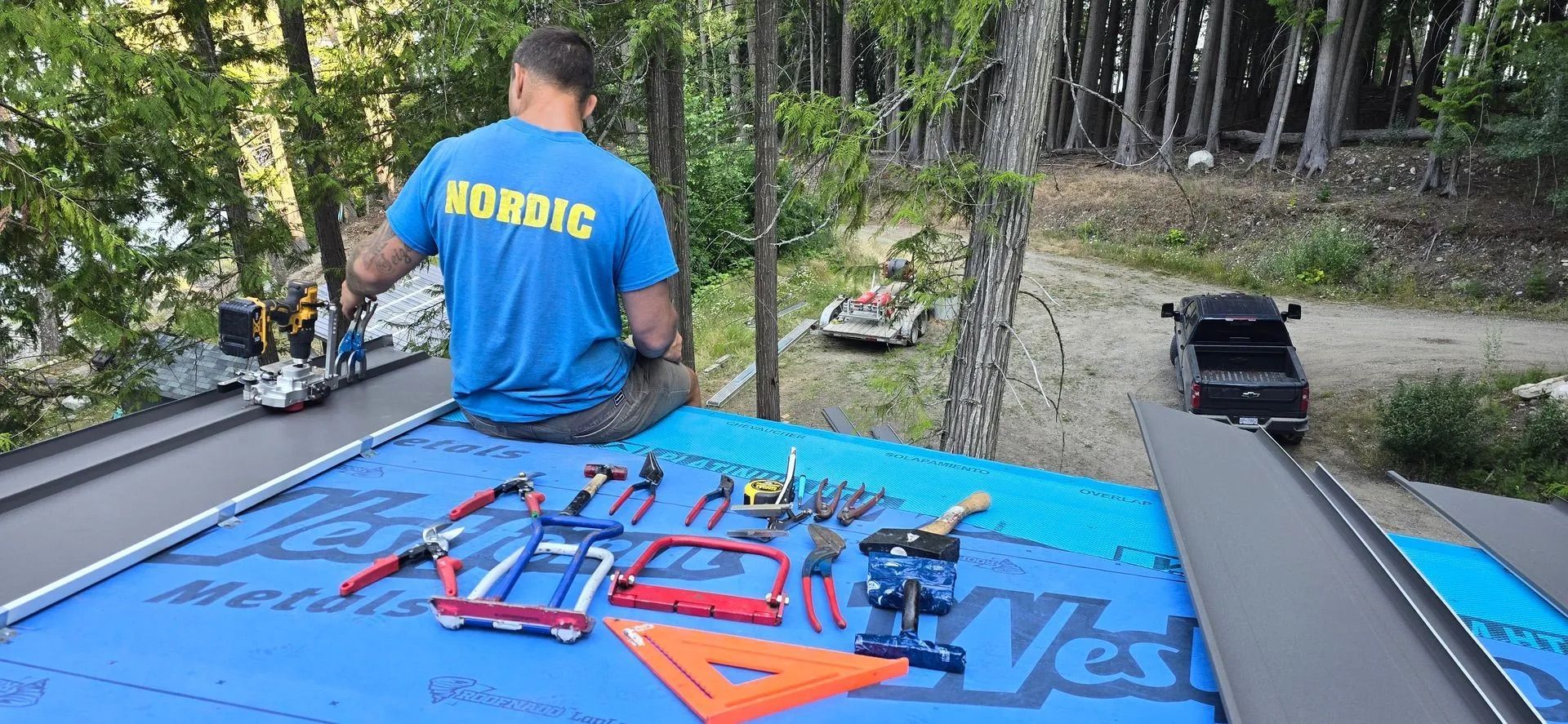 Man in blue shirt works on tools laid out on a blue tarp beside a truck in a wooded area