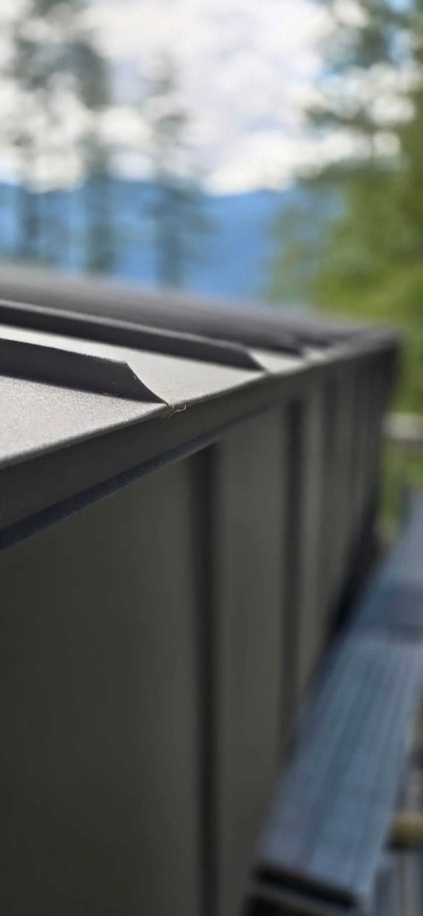 Close-up of a black rooftop edge with blurred trees and blue water in the background