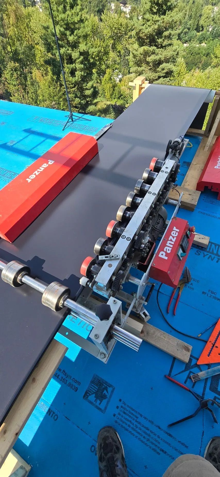 Outdoor view of a small mechanical conveyor or assembly line on a blue tarp with red components