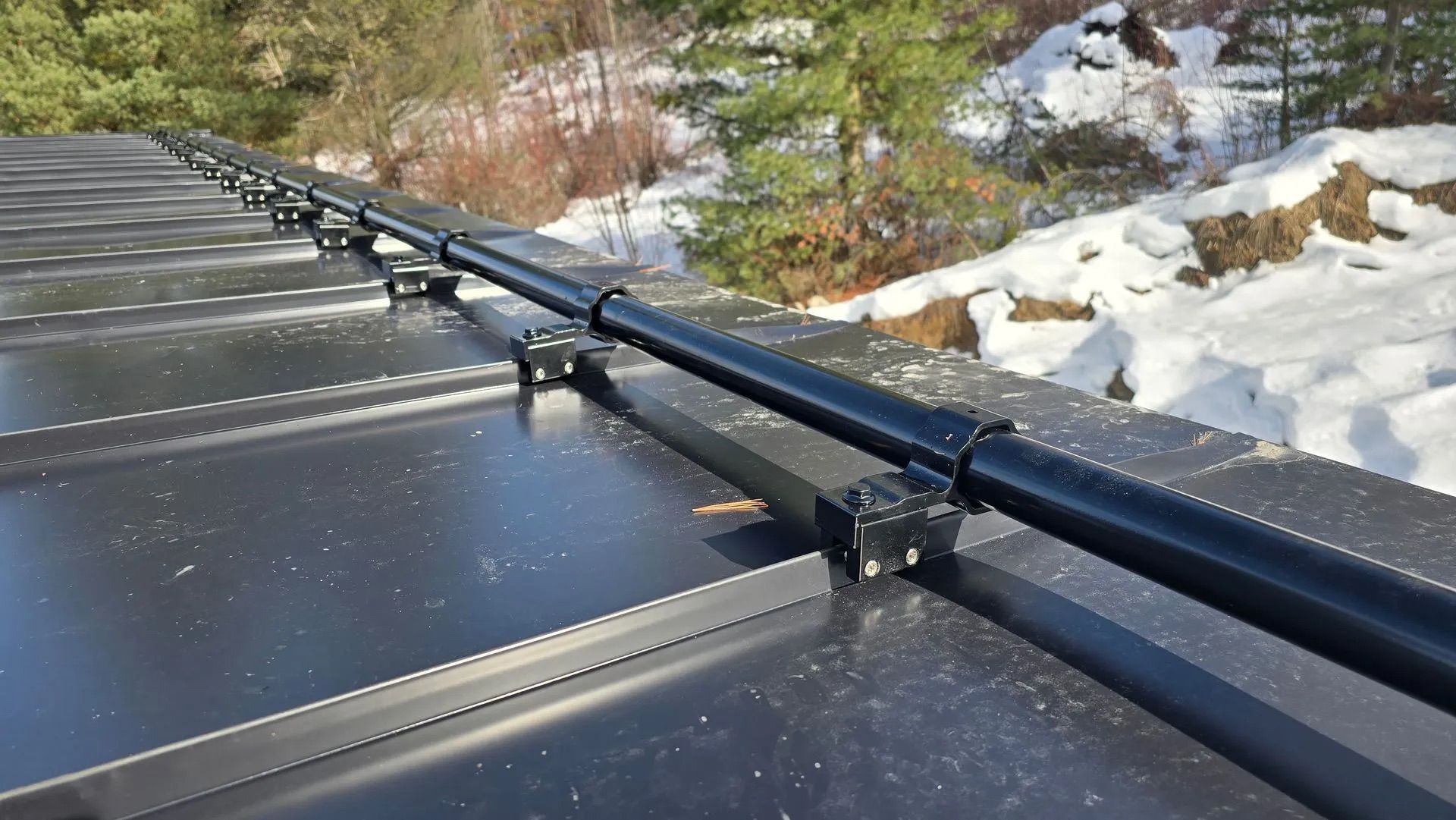 Black rooftop solar panels with mounting rails beside snow and trees