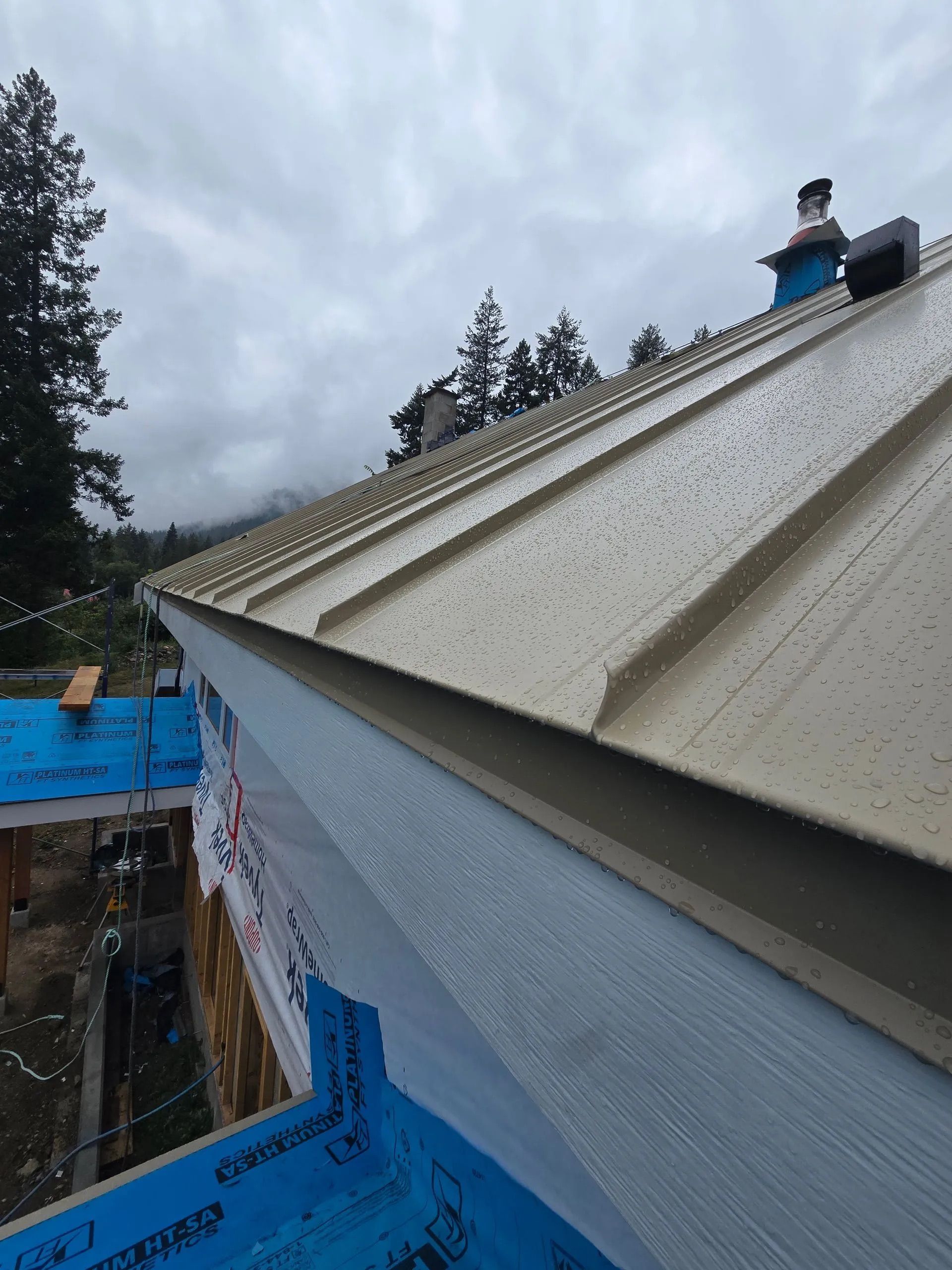 Roof under construction with tan metal panels, blue tarp, and cloudy sky
