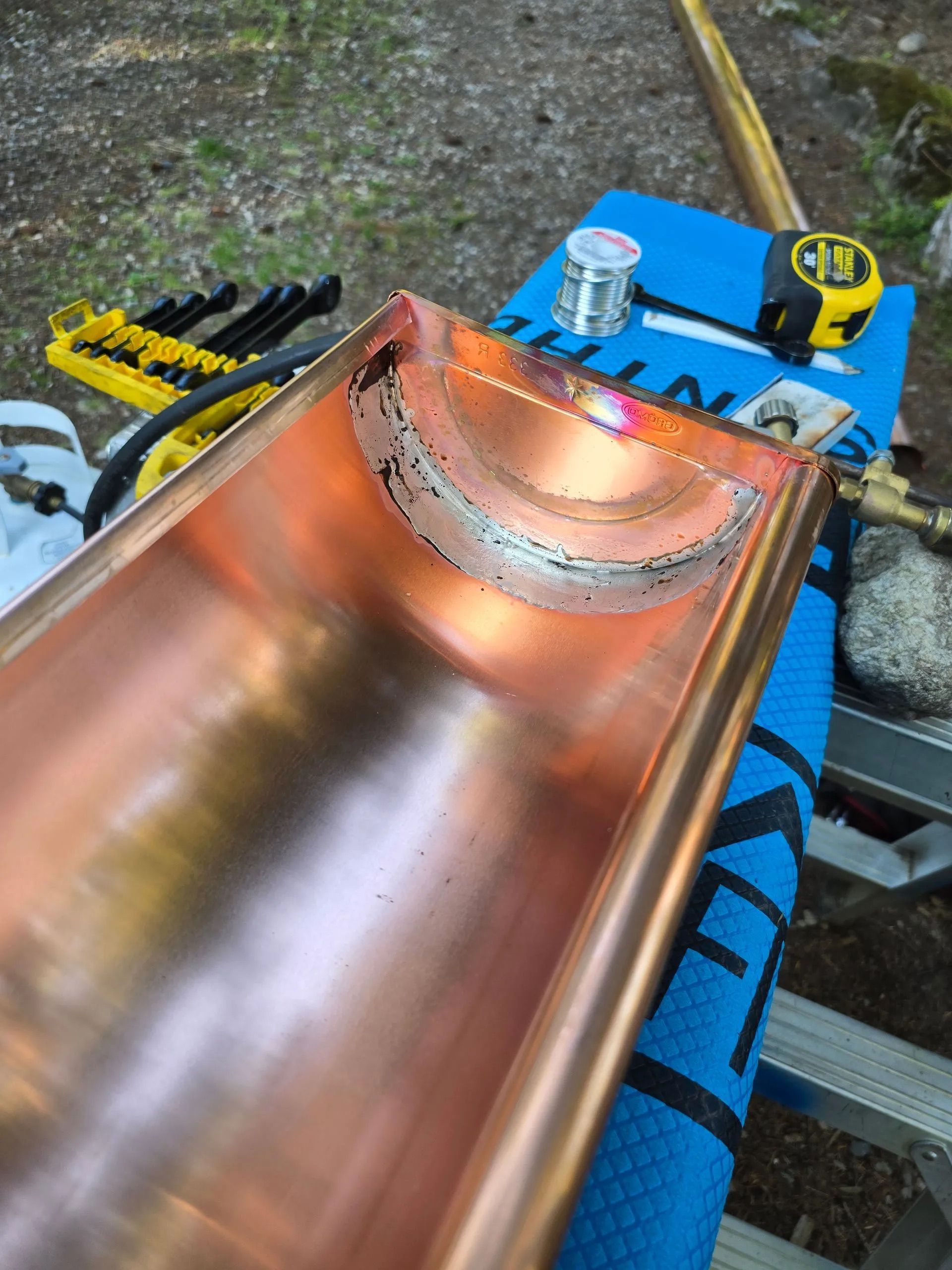 Copper-colored metal slide with a curved top section, outdoors on a work surface with tools nearby