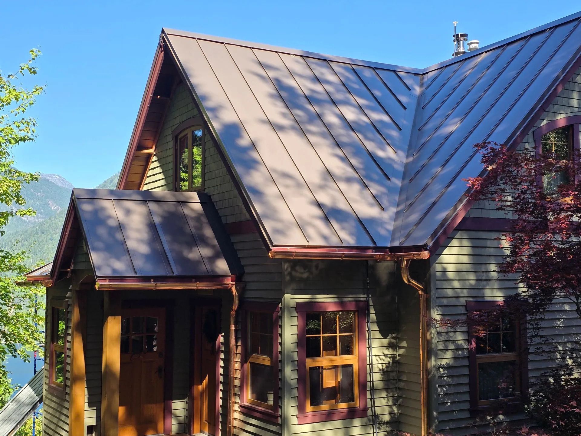 Wooden house with a steep metal roof and porch, lit by warm sunlight under a clear blue sky